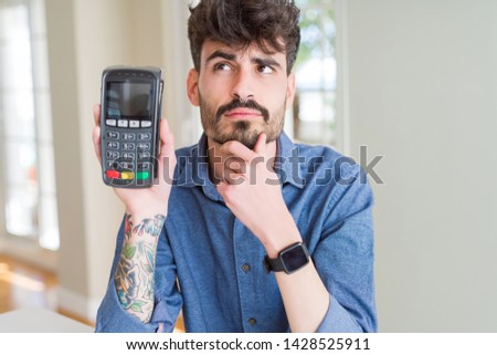 Young man holding dataphone point of sale as payment serious face thinking about question, very confused idea