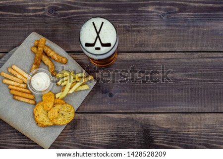 Diverse snacks and beer with silhouettes of hockey sticks on dark wooden background. Top view, Empty space for text.