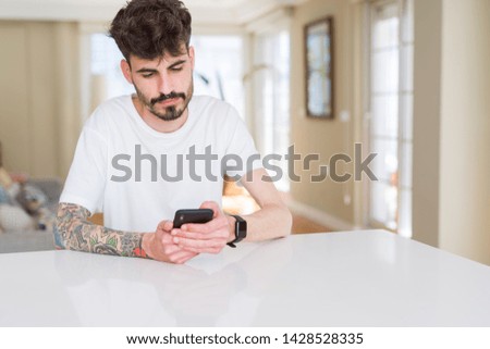 Young man with tattoo using the smartphone at home