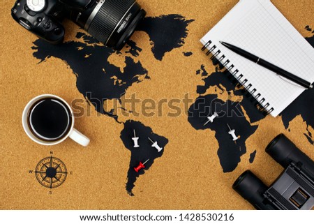 Cup of black coffee on a map with pins, camera, binoculars, notepad and pen. Top view.