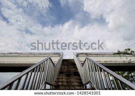 A staircase rising on a floating bridge on the background of the sky and black rain clouds.The idea of walking up the steep stairs to reach the intended destination with success and confidence.