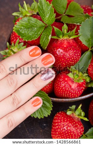 Hand with short manicured nails colored with red nail polish and strawberries