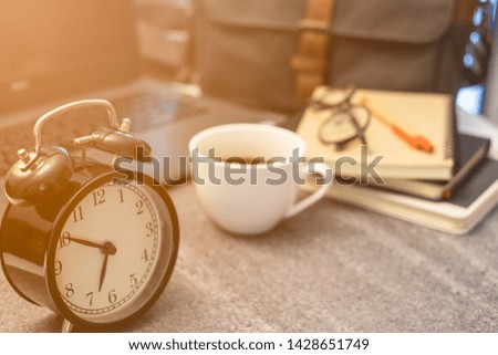 Close-up of Retro alarm black clock vintage style with white cup coffee in morning time on the top table. Wake, before go to work.