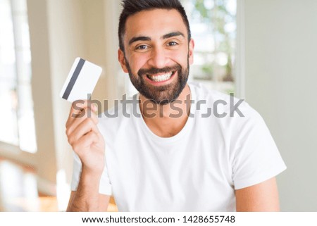 Handsome hispanic man holding credit card with a happy face standing and smiling with a confident smile showing teeth