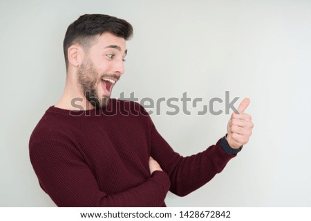 Young handsome man wearing a sweater over isolated background Looking proud, smiling doing thumbs up gesture to the side