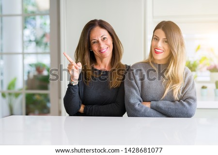 Beautiful family of mother and daughter together at home with a big smile on face, pointing with hand and finger to the side looking at the camera.