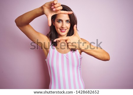 Young beautiful woman wearing striped pink swimsuit swimwear over pinisolated background smiling making frame with hands and fingers with happy face. Creativity and photography concept.