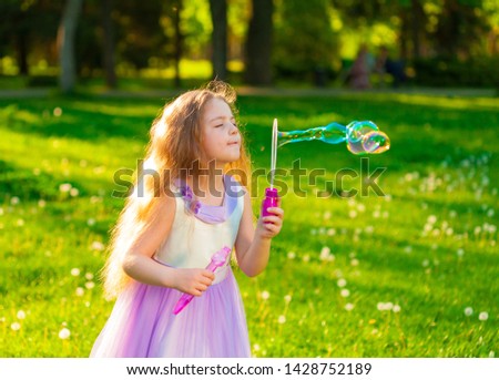 Beautiful little girl, has happy fun smiling face, long blonde pretty hair, playing soap bubbles, clothes in dress, enjoying green forest landscape. Child portrait. Kids family. Amazing panorama view.