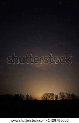 beautiful night sky with clouds and a forest on the ground with small light from the city