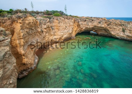 Landscape photo of a hidden cove with turquoise waters on the coast with a sunny sky with some clouds. Shot in the Faro district  in the Algarve, Portugal. 