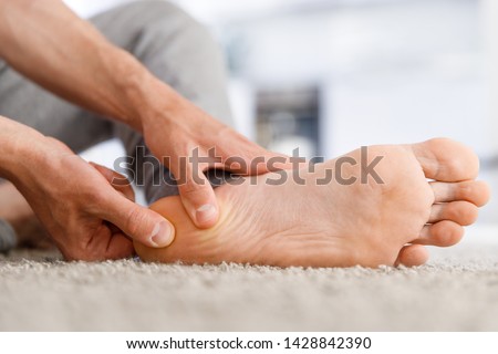 Man hands giving foot massage to yourself after a long walk, suffering from pain in heel spur, close up, indoors. Flat feet, leg fatigue, plantar fasciitis,  Royalty-Free Stock Photo #1428842390
