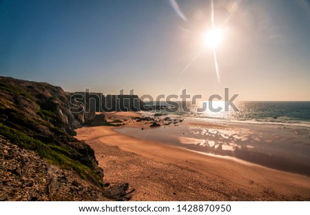 Landscape photo of a beautiful, deserted sandy beach at sunset with high cliffs in the distance. Shot in Parque Natural do Sudoeste Alentejano e Costa Vicentina near Lisbon, Portugal. 