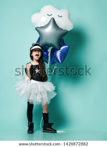 Stylish little asian girl kid in fashion skirt holds metallic balloons stars and cloud for kids birthday party and screams shouts sings songs on blue mint background