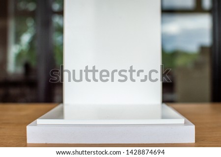 Close up picture of white product pedestal on a wooden table. Shalow depth of field, blurred background. White steps, white back plate for displaying products.