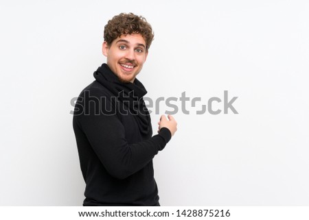 Blonde man over isolated white wall pointing back