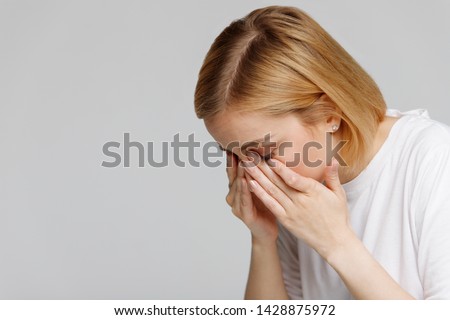 Young woman has a problem with contact lenses, rubbing her swollen eyes due to pollen, dust allergy. Dry eye syndrome, watery, itching. Isolated on grey background, free space.  Royalty-Free Stock Photo #1428875972