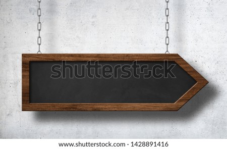 Arrow shaped blackboard hanging on chains with concrete wall