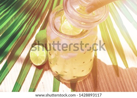 Cold fresh lemonade drink with lime slice and ice cubes in a jar on a tropical background