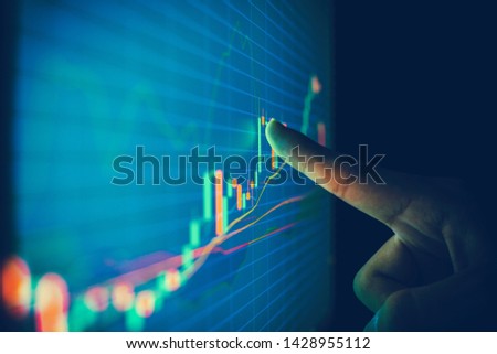 Closeup hand pointing finger on blue color monitor to analyse stock market graph Royalty-Free Stock Photo #1428955112