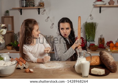 Mother and her daughter are baking a bread and having fun at the kitchen.