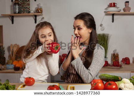 Mother and her daughter are making a vegetable salad and having fun at the kitchen.