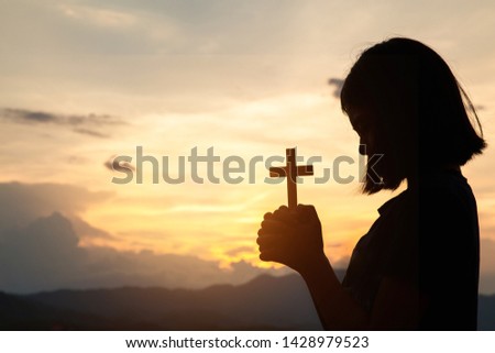Religious concepts. Silhouette of a girl holding a crucifix to God. Morning with beautiful sunrise, Symbol of Faith. Christian life prayer crisis to god.