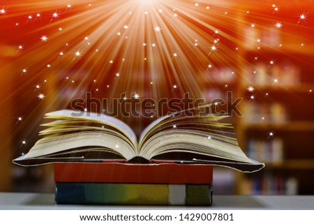 Open Book with abstract magic bright light on wooden table and blurred bookshelf in the library.