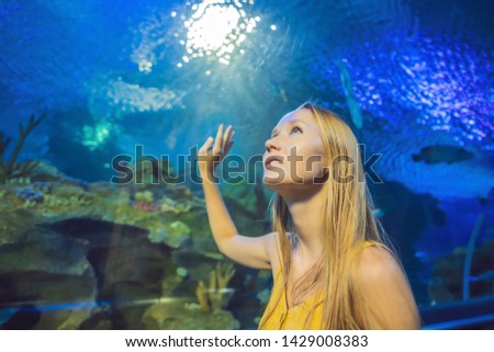 Young woman touches a stingray fish in an oceanarium tunnel