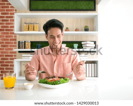 Asian young man eating salad organic health food and orange juice in the morning at the kitchen in home with white copy space Royalty-Free Stock Photo #1429030013