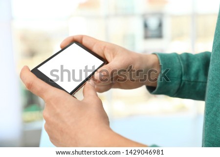 Man holding smartphone with blank screen on blurred background, closeup of hands. Space for text