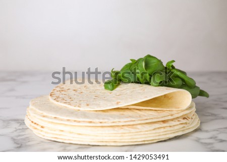 Stack of tasty tortillas with basil leaves on marble table. Space for text