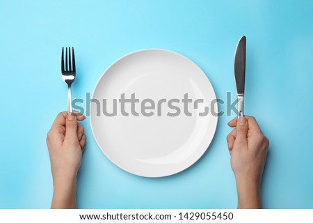 Woman with fork, knife and empty plate on color background, top view Royalty-Free Stock Photo #1429055450