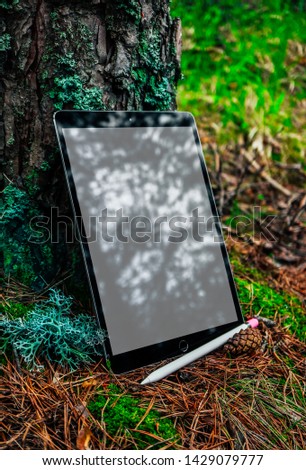 Digital tablet computer with blank screen and drawing stylus pen in a mossy forest. Mobile device mock up in a park background. Working outdoor, freelance, creation and drawing concept.