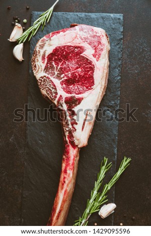 Top view of raw dry-aged marble beef steak Tomahawk on a kraft paper with spices. Flat lay, copy space, cooking concept.