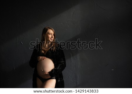 Portrait of a pregnant girl against a black wall