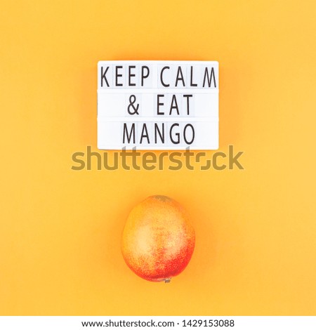 Mango fruit in creative conceptual top view flat lay composition with lightbox with Keep calm and eat mango slogan isolated on orange background in minimal style with copy space. Pop art poster