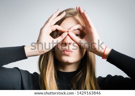 beautiful blonde woman showing binoculars with her hands, isolated on background