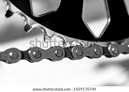 Dark metallic chain of a Bicycle filmed in close up. small details are visible. The background is blurred.