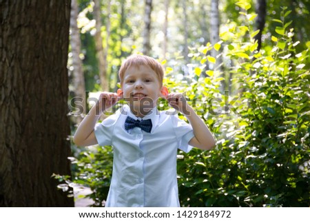Yong little white redheaded boy makes faces against a summer park. Portrait of a happy boy who makes funny faces outdoor.