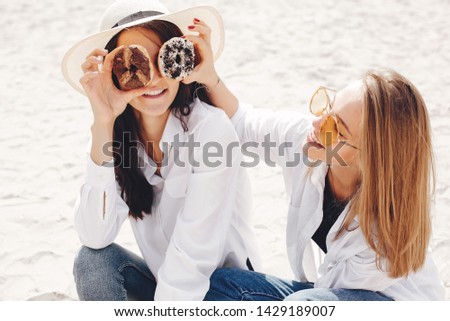Beautiful girls on a beach. Friends have fun in a summer park. Ladies sitting on the sand with a donuts