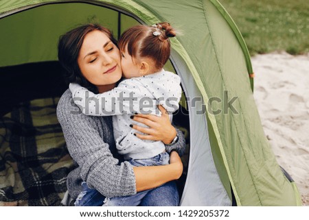 Family in a summer park. Mother in a gray sweater. Cute little girl near the tent