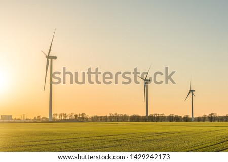 Picture of wind farm generators in the green field close to the road with cars at the sunset