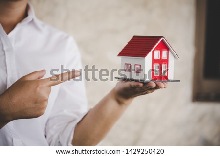 businessman in white shirt holding a small house in hand 