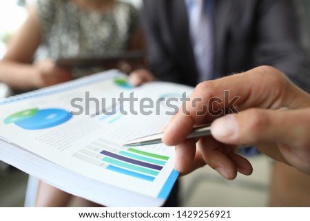 Male hand hold silver pen with chart aganist group business people background. Financial statistic analisis concept.