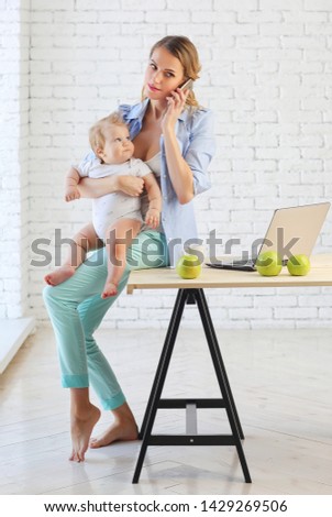 A young mother in the kitchen talking on the phone and holding her 9-month-old child