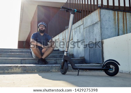 adult man sitting in front of his electric scooter, with beard and helmet Royalty-Free Stock Photo #1429275398