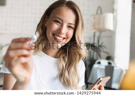 Beautiful young blonde woman sitting at the cafe indoors, listening to music with earphones