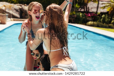 Joyful girls sitting on their friends shoulders and fighting in a pool. Group of women playing in the swimming pool on a summer day.