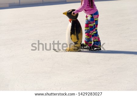 Closeup of young girl on the figure skates with learning penguin outdoor in sunny spring day