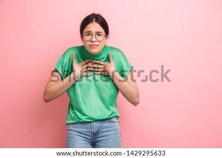 Photo of charming young girl wearing round eyeglasses touching her chest isolated over pink background